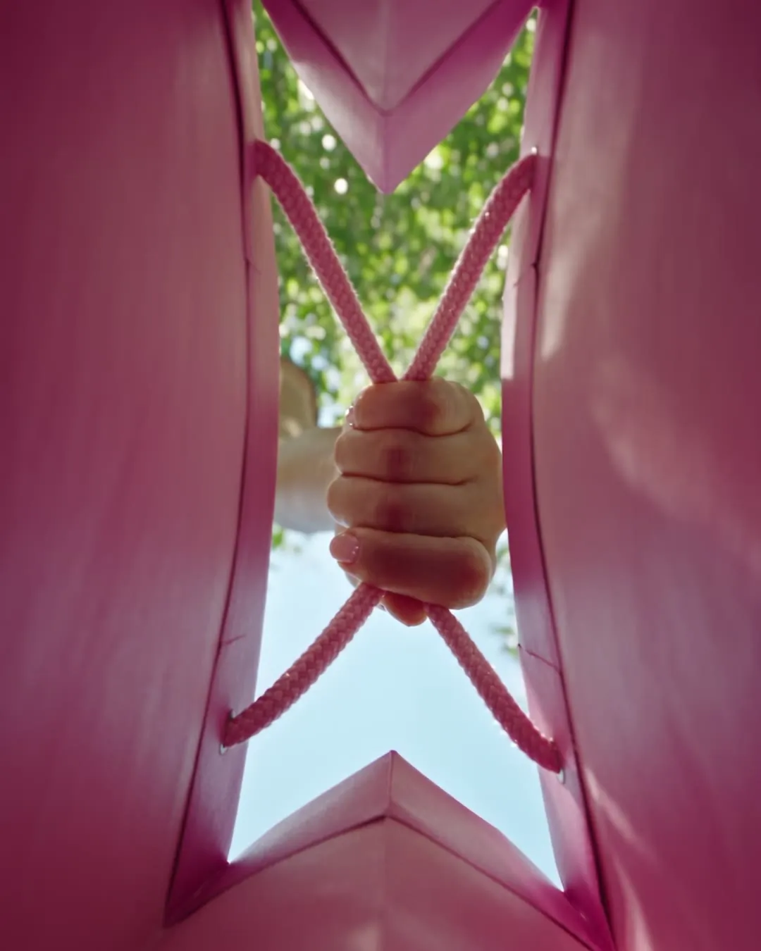 POV from the bottom of a pink paper bag looking up at hands and summer sky.